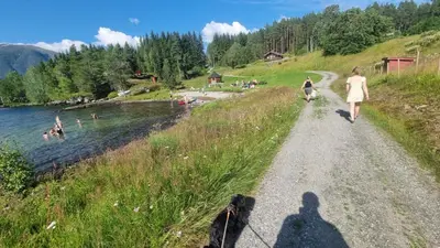 a shadow of a woman walking a dog on a path next to a lake at Skogshytte in Holmøyane