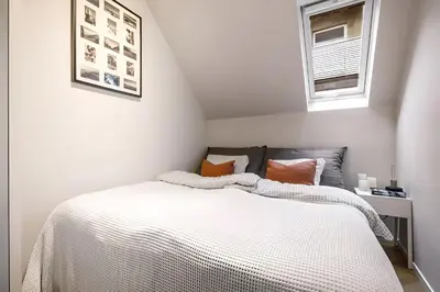 a bedroom with a bed with white sheets and two windows at Bright Top-Floor Apartment with Sea View in Bergen
