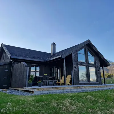 a black house with windows and chairs in a field at Mountain Cabin With Sauna In Sunnmørsalpane in Brunstad