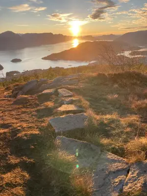 a sunset on a hill with rocks and a body of water at Petersstova in Ålesund
