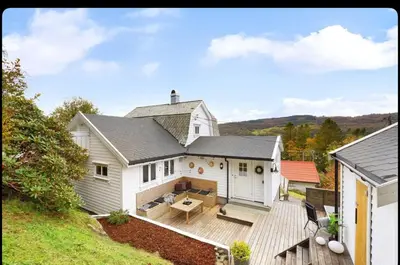 a white house with a deck with a table at Vestlandsidyll ved sjøen & Bergen