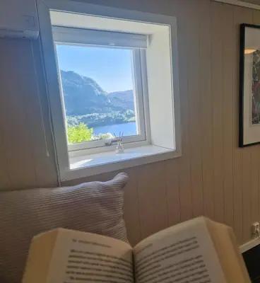 an open book sitting on a bed with a window at Cozy flat with lake view and 15 min from Bergen in Bergen