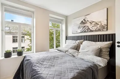 a bedroom with a large bed and two windows at Apartment Lademoen Trondheim in Trondheim