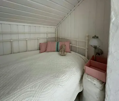 a small bedroom with a white bed with pink pillows at Historic Cabin By The Atlantic Ocean Road in Vevang