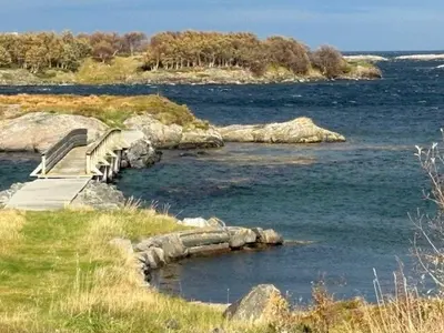 a bench on a path next to a body of water at Historic Cabin By The Atlantic Ocean Road in Vevang