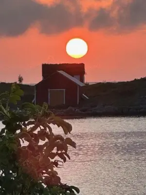 a sunset over a house with the sun in the background at Historic Cabin By The Atlantic Ocean Road in Vevang