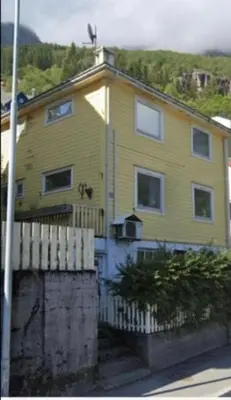 a yellow house with a fence in front of it at Green apartment in Odda