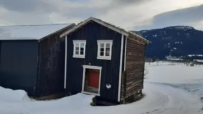 a small blue building with a red door in the snow at Trivelig Stabbur på Lånke Gård