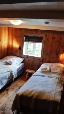 two beds in a room with wooden walls and a window at Trivelig Stabbur på Lånke Gård