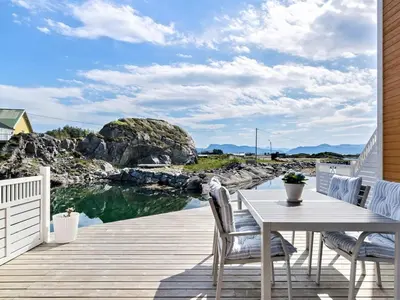 a wooden deck with a table and chairs next to a body of water at 8 person holiday home in Sandøy in Finnøy
