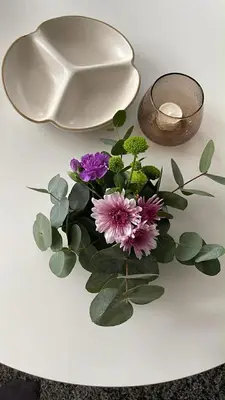 a white table with a vase and flowers on it at Bright & Spacious Apartment by the Sea, Free Parking, 10min to Airport, 12min to Ålesund in Ytterland