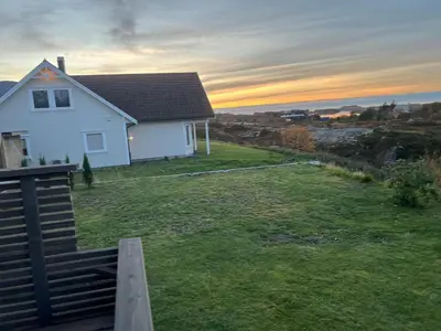 a white house on a lawn with the sunset in the background at Atlantis cabin with sauna and great views in Vevang