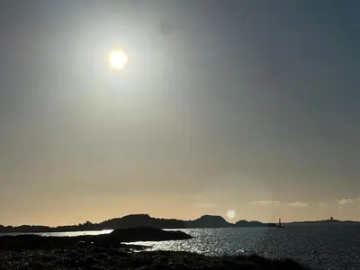 a sun setting over the water with a sail boat at Atlantis cabin with sauna and great views in Vevang