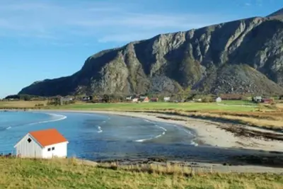 a house on the shore of a beach with mountains in the background at Atlantis cabin with sauna and great views in Vevang