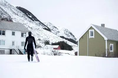a man walking in the snow holding a snowboard at Beach apartment with unique view in Ervik