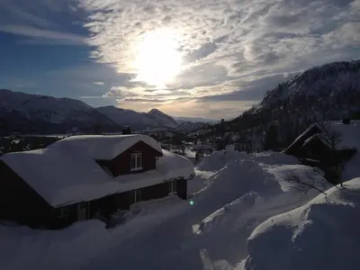 a house covered in snow with the sun in the background at Hovden Fjellpark 71 in Hovden