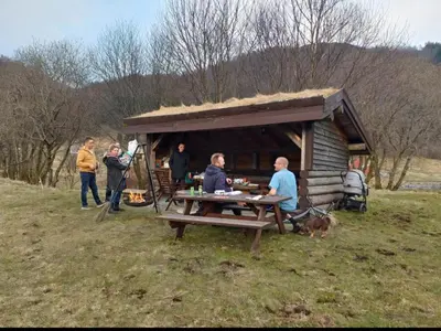a group of people standing around a picnic table in front of a hut at Nesvika 5 bedroom holiday home, only 25 min from Bergen in Bergen
