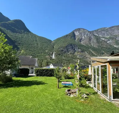a yard with a house and mountains in the background at Flåm Tinyhouse with a Waterfall View in Flåm