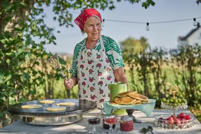 an older woman holding a spatula next to a table with cookies at Stangeland Gard in Austevoll