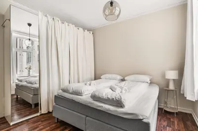 a bedroom with a bed with white sheets and a mirror at BB Apartments I 300m to Bryggen & Train Station in Bergen