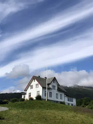 a white house on a hill with a cloudy sky at Stall Rygg Apartment, Gloppen