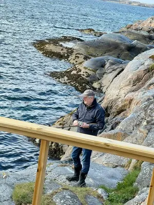a man sitting on the rocks near the water at Architectural Gem On Rocks In Kvenvær in Kvenvær