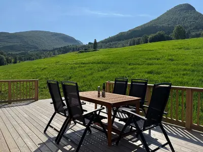 a wooden table and four chairs on a deck with a field at Living in a Nikolai Astrup motif 96m2 in Vassenden