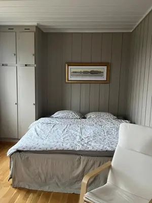 a bedroom with a bed and a white chair at Leilighet nær Color Line i Larvik in Lii