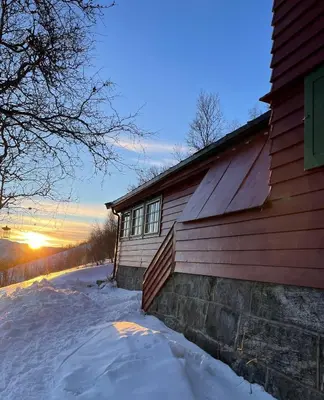 a building with the sun setting in the background at Bloksberg - cabin with amazing view and ski inn-out in Geilo
