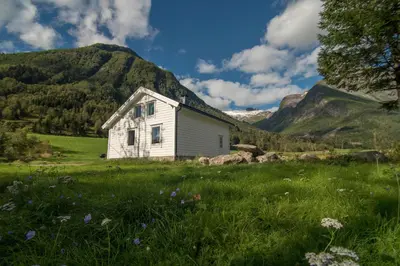 a white house in a field with mountains in the background at Hansali Holiday Home in Fjarland