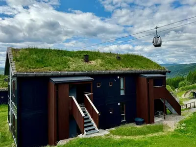 a building with a grass roof with a ski lift at Ski-In Out apt Hafjell - Sauna and Stunning Views in Hafjell