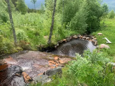 a stream of water with rocks in a field at Beautiful place among forests and fields in a good old style in Eggedal