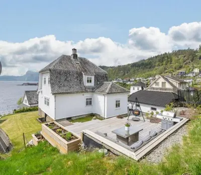 a white house with a deck next to the water at The View in Sauda