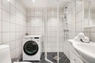 a white tiled bathroom with a washing machine in it at Central & Modern Apartment in the Coziest Street in Bergen in Bergen