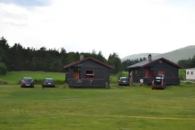 two cabins in a field with cars parked in front at Mogard in Skjåk