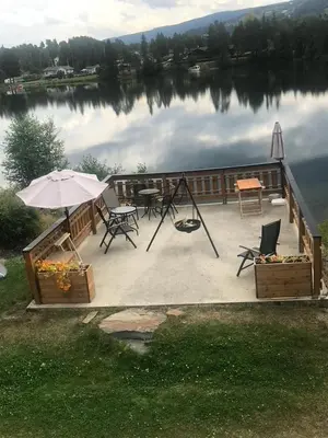a patio with a table and an umbrella on a lake at Glampingtelt i fjordkanten, Rønlund Hyttepark in Ron