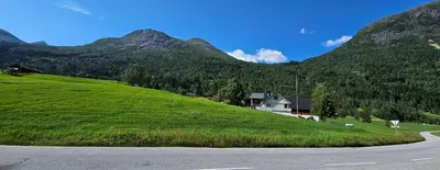 a green hill with a house on the side of a road at Lakeside apartment in Stryn