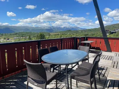 a table and chairs on a deck with a view of mountains at Stor Toppleilighet I Sentrum in Beitostøl