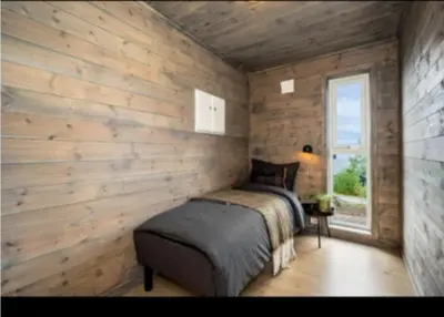 a bedroom with wooden walls and a bed and a window at Cabin at the end of Skardsøya towards the sea - boat in Bukta