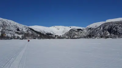 a person walking across a frozen lake with snow covered mountains at Spacious Wood Cabin 50 min from Bergen in Eikedalen