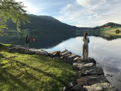 two people standing on a rock wall near a lake at West coast peace in Hyllestad