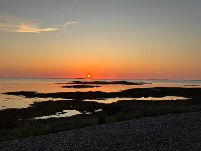a sunset over the ocean with rocks in the water at Et hus dypt i havet in Steinshamn