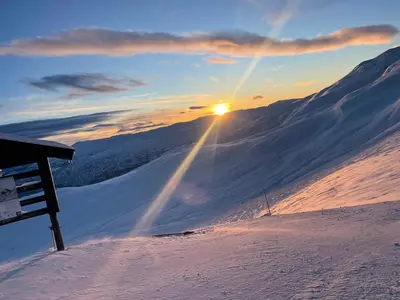 a sunset on a snow covered mountain with the sun shining on the horizon at Apartment vårstølen in Vossevangen