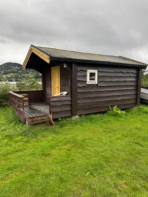 a small cabin with a wooden porch and a yellow door at Sjøbakken Fjord Camping AS in Sykkylven