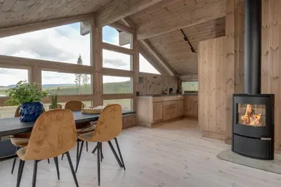 a living room with a fireplace and a table and chairs at Hedda Robølshøvda - 3 bedroom cabin with a lovely view in Heggenes