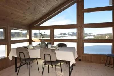 a dining room with a table and chairs and windows at Hedda Robølshøvda - 3 bedroom cabin with a lovely view in Heggenes