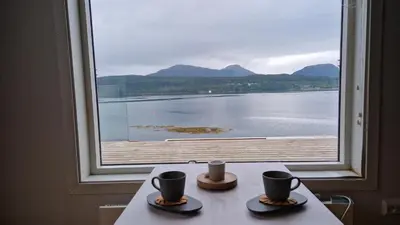 a table with two cups and a large window at Seaside cabin with stunning view! in Ålesund