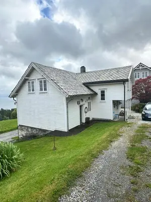 a white house with a car parked in the driveway at Cozy older house in scenic surroundings in Stord
