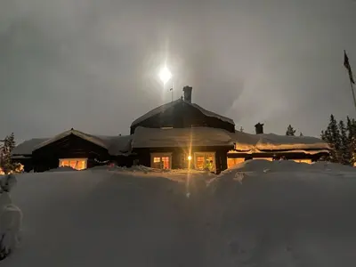 a house covered in snow at night with a light on top at Stor velutstyrt laftehytte med usjenert uteplass, flott utsikt og Jacuzzi in Eggedal