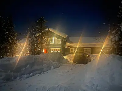 a house with a car parked in the snow at night at Stor velutstyrt laftehytte med usjenert uteplass, flott utsikt og Jacuzzi in Eggedal